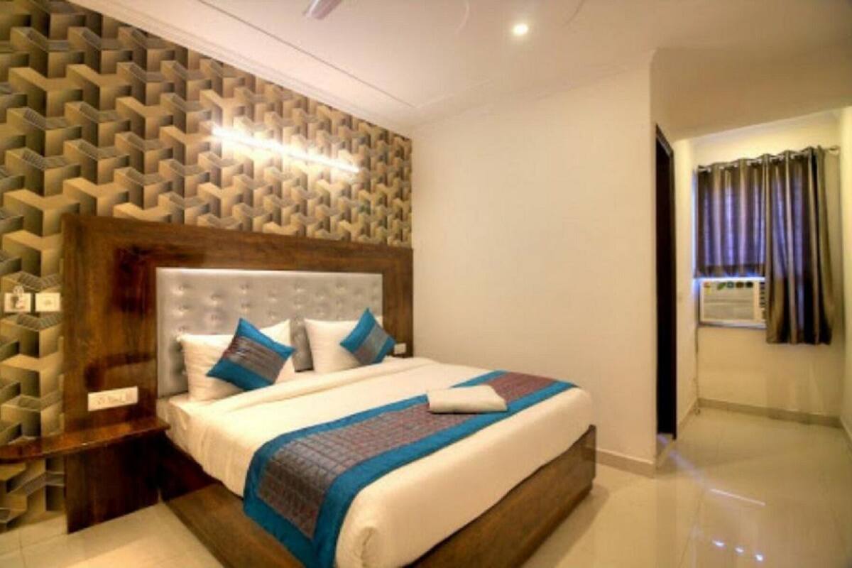 A hotel room with a patterned wall, a large bed with pillows, a nightstand, and a window with curtains.