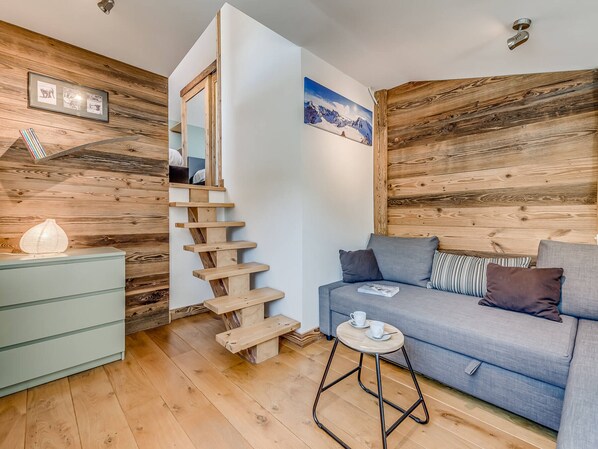 Un salón moderno con una escalera de madera, un sofá gris y una pequeña mesa redonda con tazas.