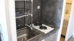 Une petite cuisine équipée avec un évier en acier inoxydable, un égouttoir à deux niveaux et une plaque de cuisson intégrée.