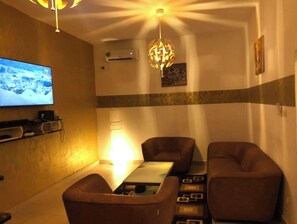 Un salon moderne doté d’un téléviseur à écran plat, d’une table, de deux canapés et d’un luminaire décoratif.