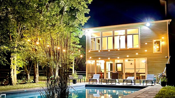 Una casa moderna con piscina, rodeada de árboles y luces colgantes.
