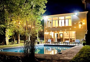 Een modern huis met een zwembad, omringd door bomen en lichtjes.