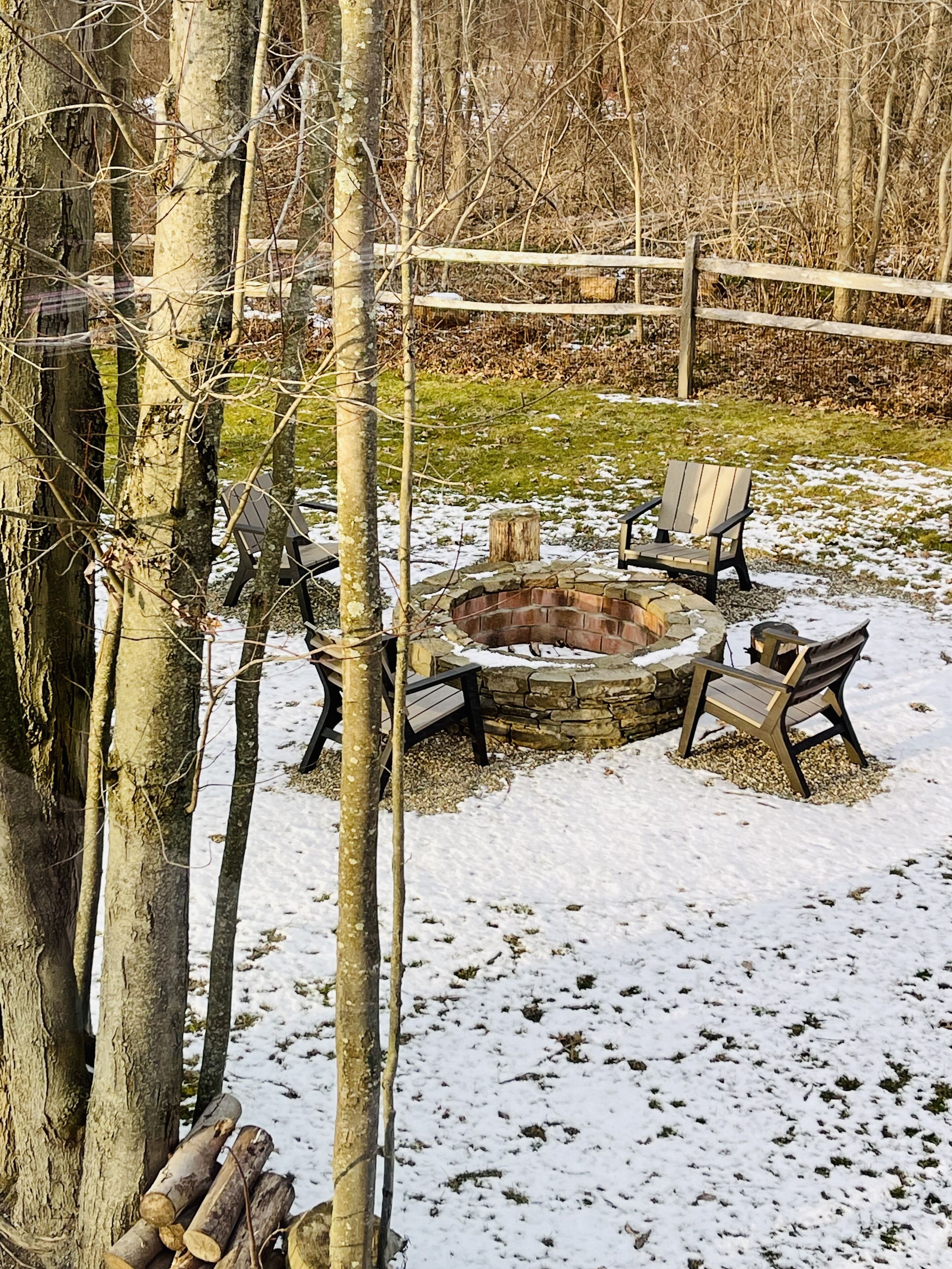 A fire pit with chairs around it, surrounded by trees and a wooden fence.