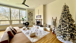 Una sala de estar acogedora con un ventanal grande, una chimenea, un árbol de Navidad y un ventilador de techo moderno.