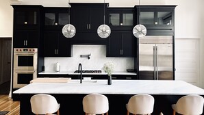 Una cocina moderna con armarios oscuros, una isla central, electrodomésticos de acero inoxidable e iluminación colgante.