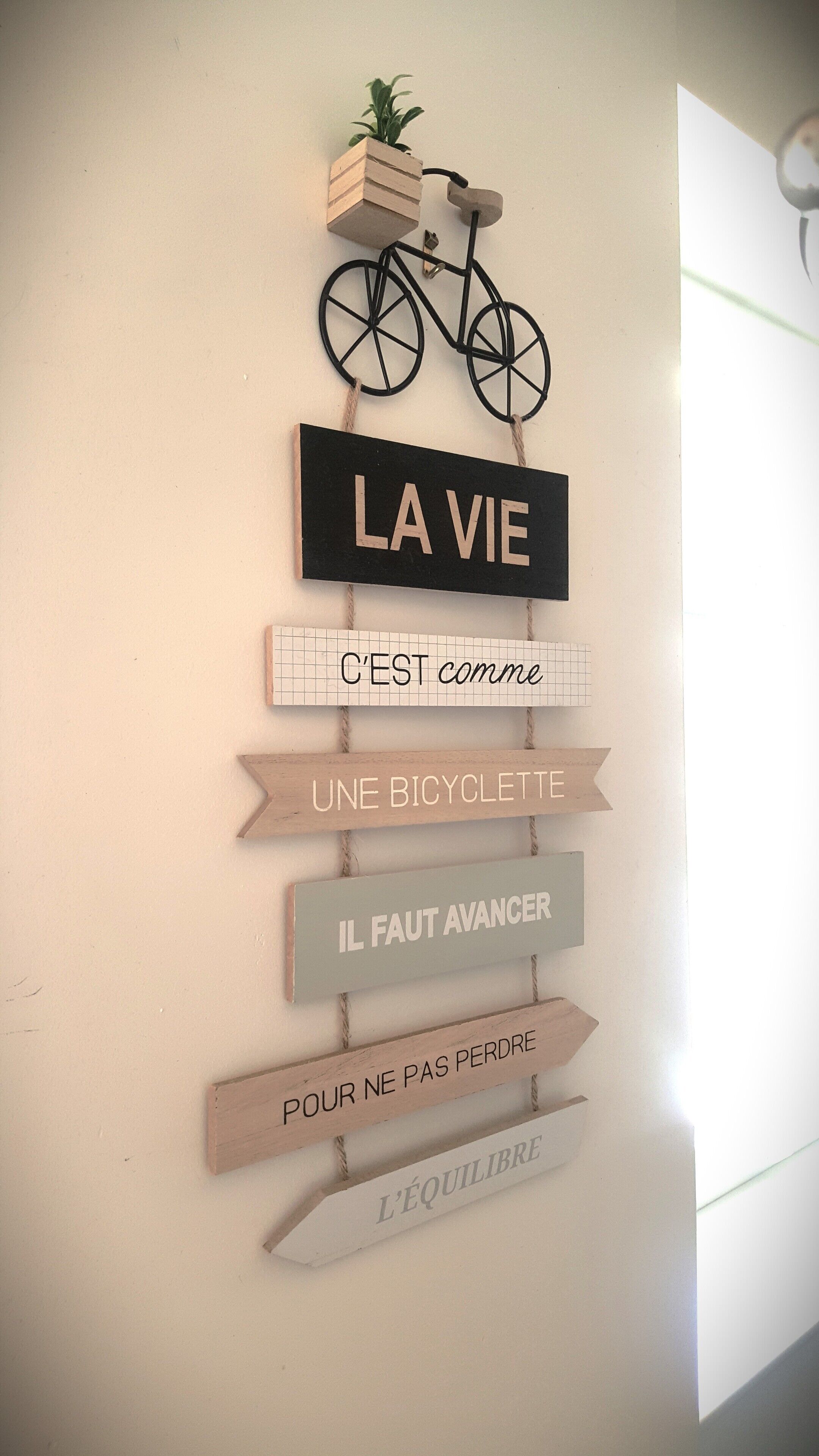 Un cartello appeso al muro con una bicicletta e testo in francese, probabilmente a scopo motivazionale o decorativo.