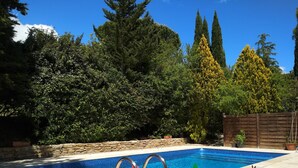 A swimming pool with a red inflatable float, surrounded by lush greenery and tall trees. - Independent bedroom, swimming pool, Park, Kitchen, Barbecue... (Brézilhac)