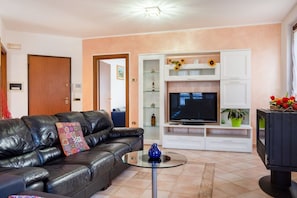A living room with a black leather sofa, a glass coffee table, a flat-screen TV, and a white entertainment unit with shelves.