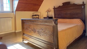 A bedroom with a wooden bed, a nightstand, a chair, and a window with blinds. - QUIET STONE HOUSE 3KMS FROM THE BEACH (La Foret-Fouesnant)