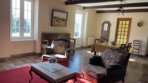 A spacious living room with a fireplace, two armchairs, a dining table, and a large window. - QUIET STONE HOUSE 3KMS FROM THE BEACH (La Foret-Fouesnant)