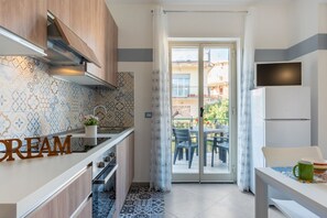 A modern kitchen with patterned tiles, a wooden cabinet, a countertop with a 'CREAM' sign, a sliding glass door to a balcony, and a dining table with chairs. - GuestHost - Comfortable and modern 40 sqm apartment with balcony, for 4 people, located on the first floor of a building (NO elevator) inside the Sileno Beach residential complex. The property is located in a central position, a few minutes on foot from  (Giardini Naxos)