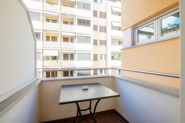 Un balcón con una mesita y una ventana con vistas a un edificio de varios pisos.