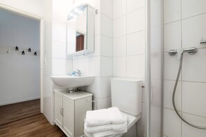 A modern bathroom with a white sink, mirror, and toilet. There is a shower area with a glass door and a towel rack with white towels.