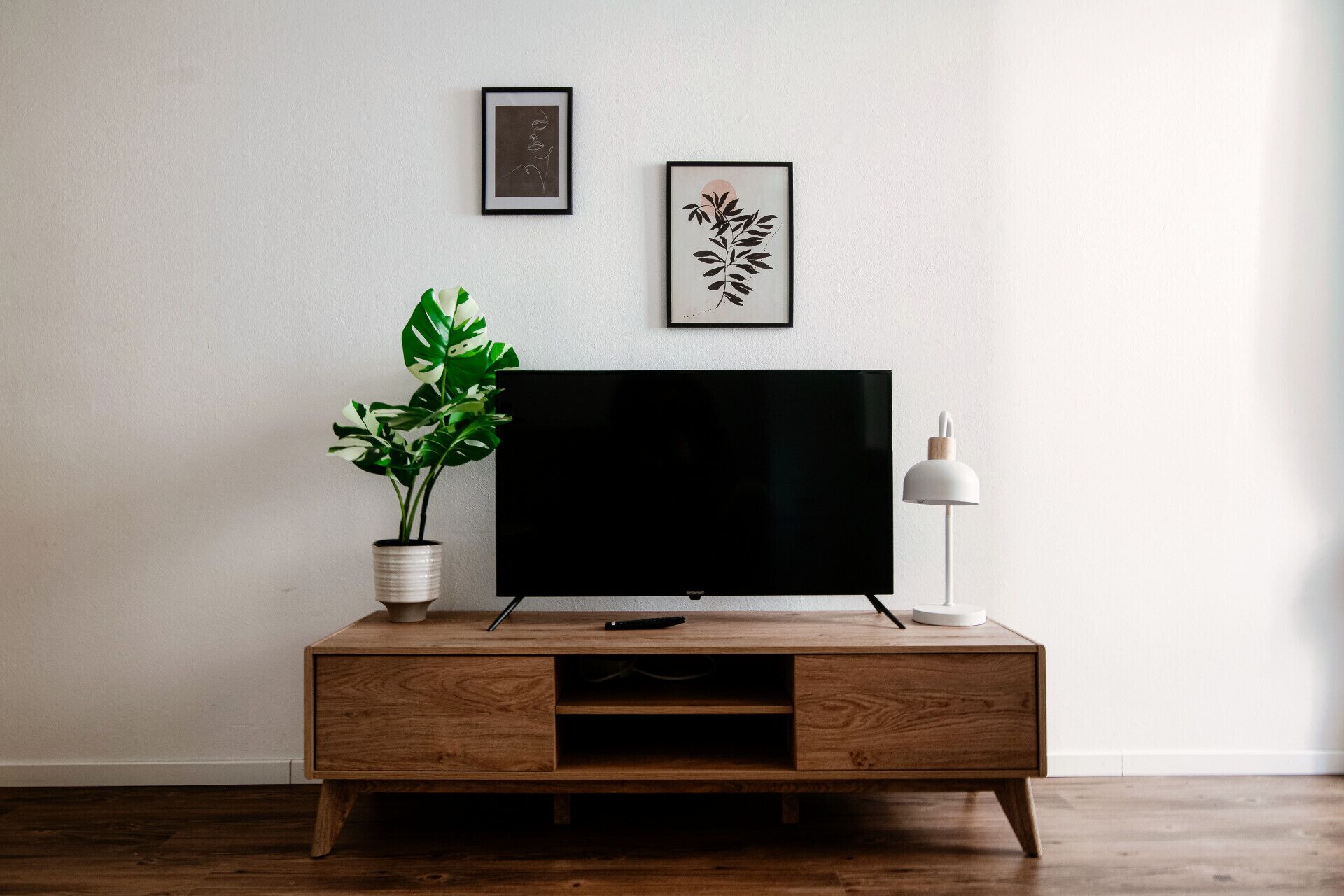 Un meuble en bois pour la télévision, sur lequel est posée une télévision à écran plat, ainsi qu’une plante en pot et une lampe sur pied.