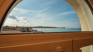 Vista a través de una ventana de marco curvo, que da a una zona costera con edificios y una isla distante.