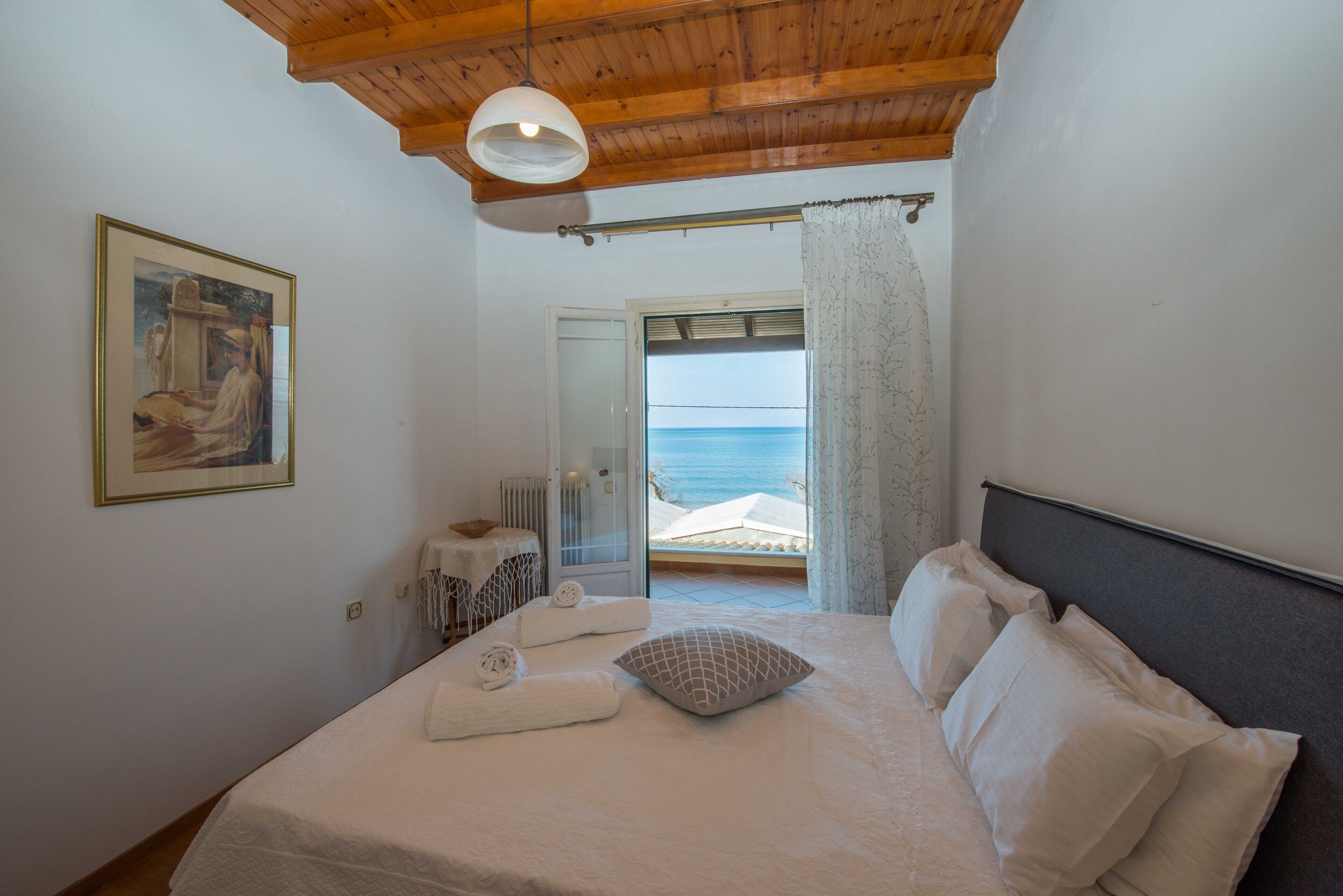 Un dormitorio con cama, un cuadro en la pared y vista al mar a través de una puerta abierta.