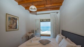 Un dormitorio con cama, un cuadro en la pared y vista al mar a través de una puerta abierta.