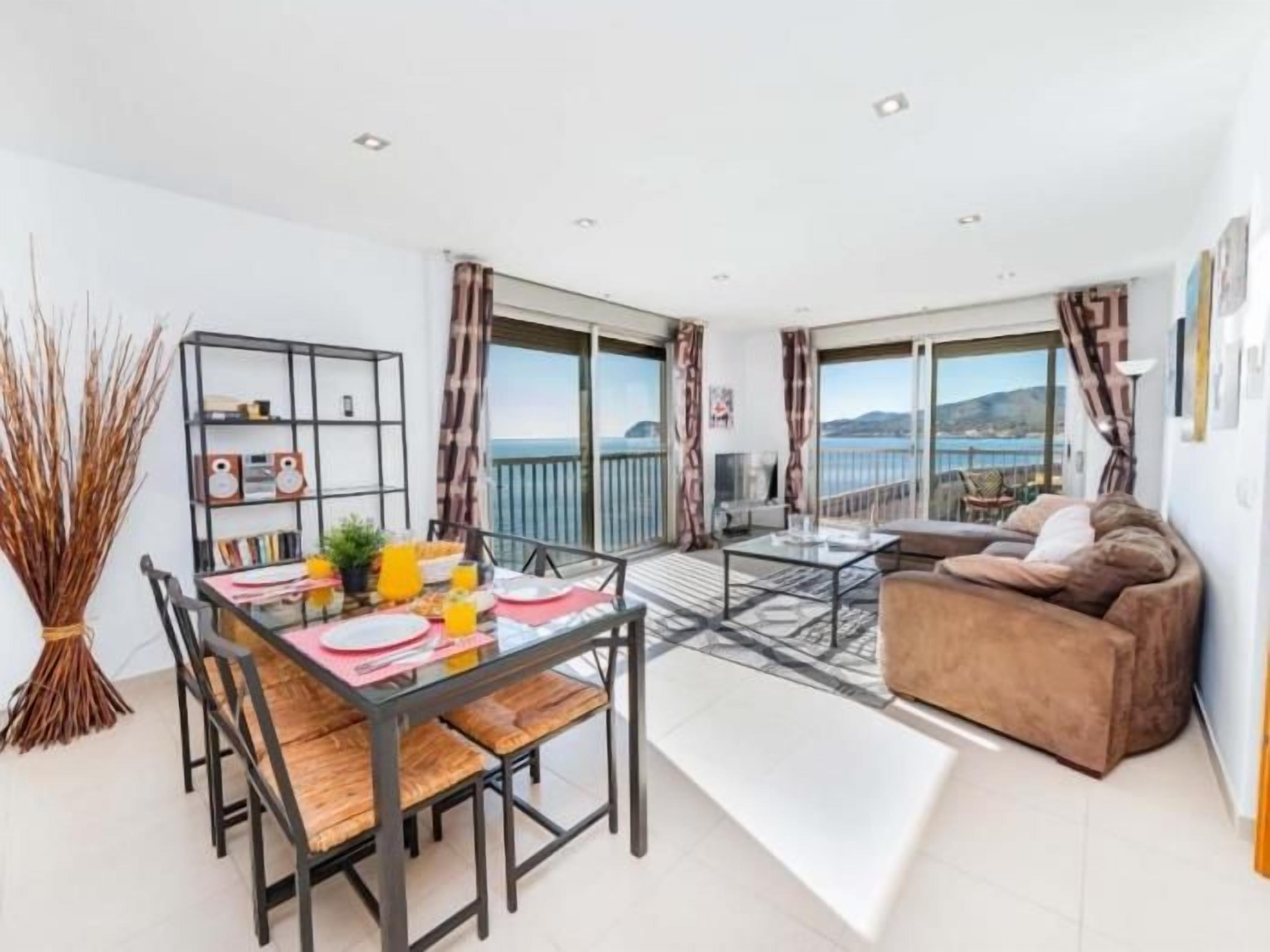 A modern living room with a dining area, a sofa, and a balcony with a view.
