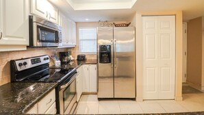A modern kitchen with stainless steel appliances, white cabinetry, and a black granite countertop.