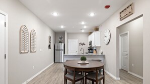 Una cocina moderna con armarios blancos, un refrigerador de acero inoxidable y una zona de comedor con mesa y sillas de madera.