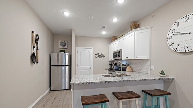 Una cocina compacta con refrigerador, microondas, pileta y taburetes de bar.