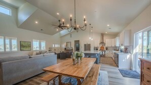 A spacious living room with a large wooden table, a grey sofa, and a chandelier. - Brand-new Farmhouse Style Ranch w/Fire Pit in the heart of Paso Robles! (Paso Robles)