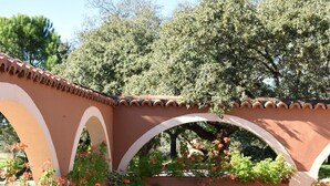 A swimming pool with a blue cover, surrounded by brick flooring and arches with potted plants.