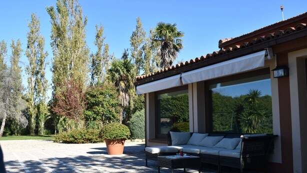 A covered outdoor seating area with a sofa and coffee table, surrounded by potted plants and trees.