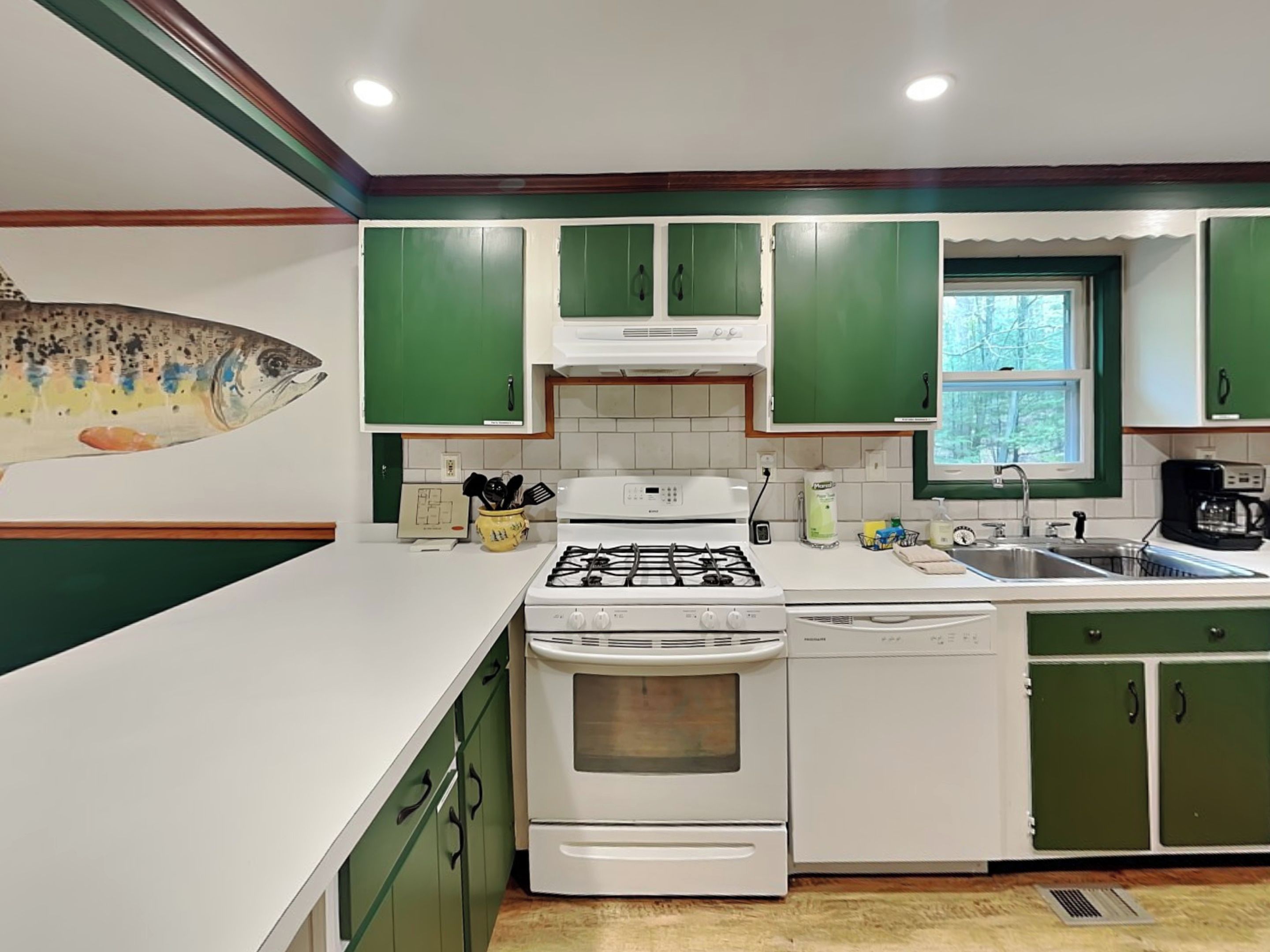 Una cocina con armarios verdes, una estufa blanca y una ventana con vistas a árboles.