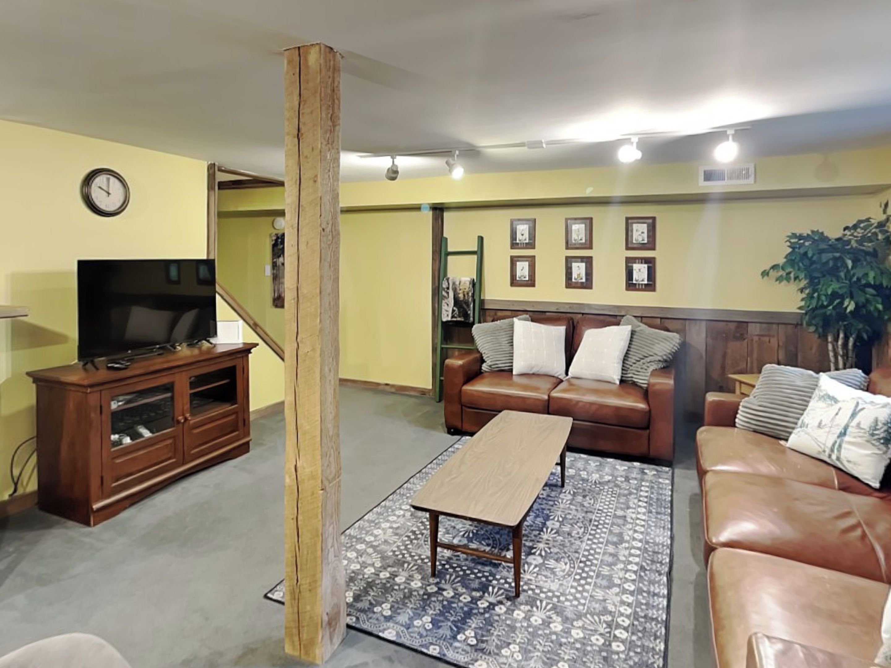 Una sala de estar con un sofá de cuero marrón, una mesa de centro de madera, un televisor sobre un mueble de madera y una alfombra estampada.