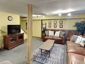 Una sala de estar con un sofá de cuero marrón, una mesa de centro de madera, un televisor sobre un mueble de madera y una alfombra estampada.