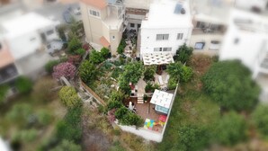 An aerial view of a residential area with multiple buildings, a small garden with various plants, and outdoor seating areas. - Villa Ariadni Crete (Agios Vasileios)