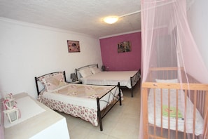 Quarto com duas camas, um berço, uma mesinha de cabeceira e um criado-mudo.
