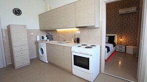 A compact kitchen with a washing machine, stove, and microwave. - Villa Ariadni Crete (Agios Vasileios)