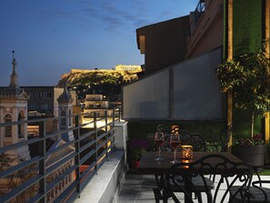 Une terrasse avec une table dressée pour deux personnes, offrant une vue sur le paysage urbain, avec ses bâtiments historiques et une forteresse perchée sur une colline.