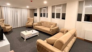 A living room with a sofa, armchairs, a coffee table, and a TV stand. - Şimal Hotel (Rize)