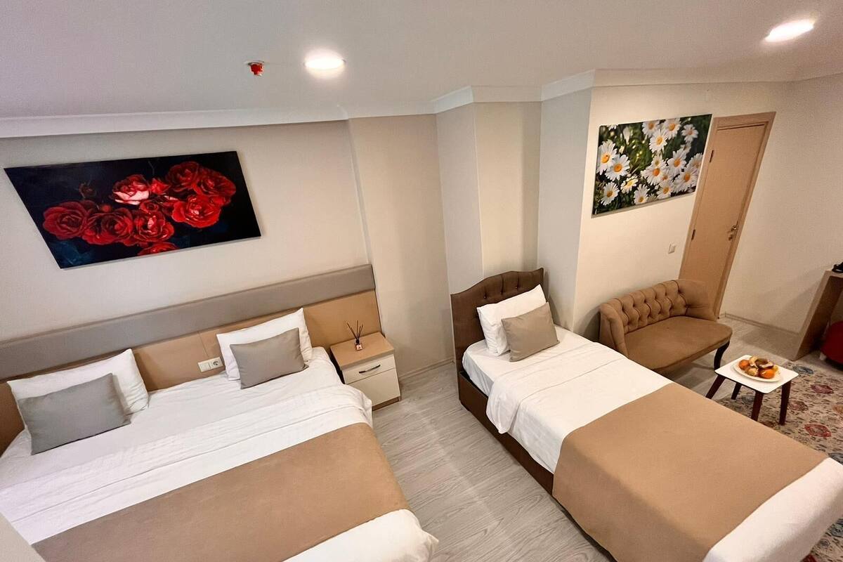 A hotel room with two beds, a small table, a chair, and artwork on the walls.