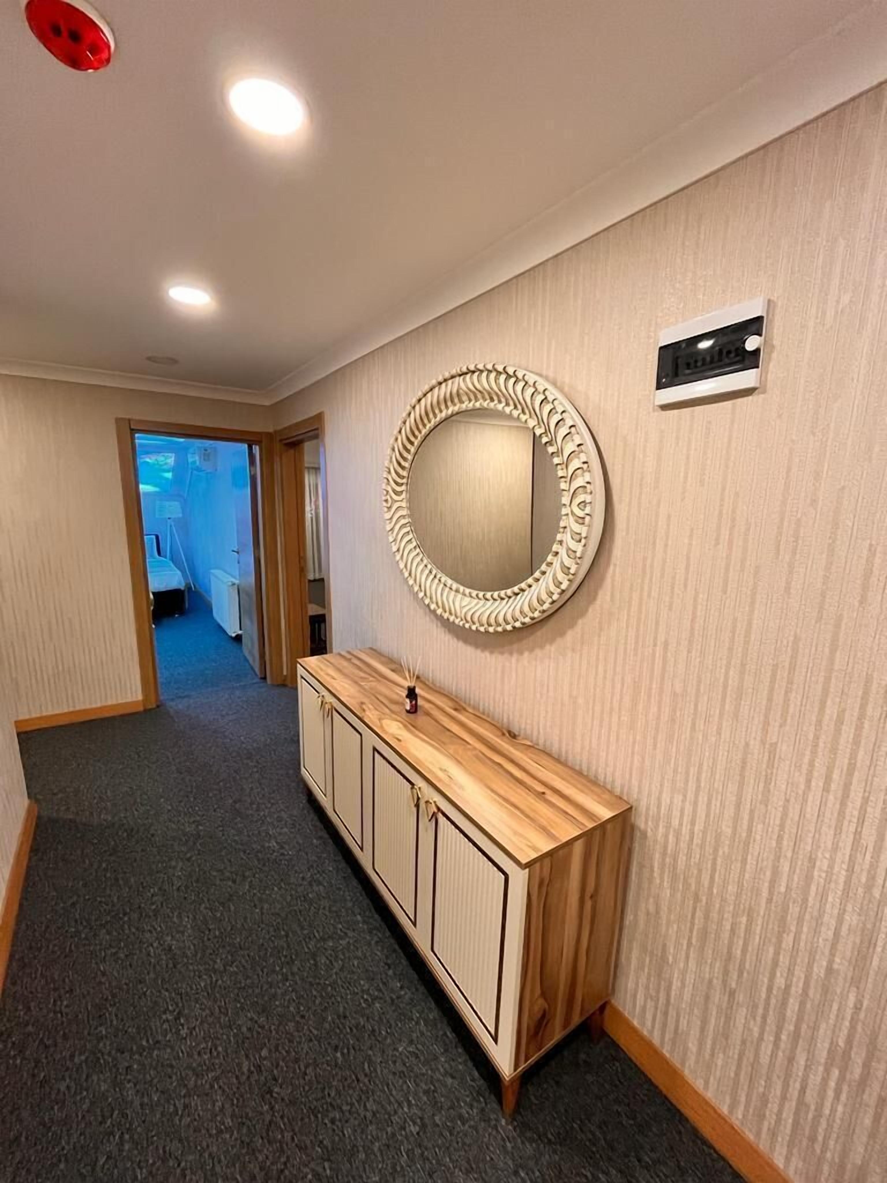 A hallway with a wooden vanity, a round mirror, and a wall-mounted air conditioning unit.