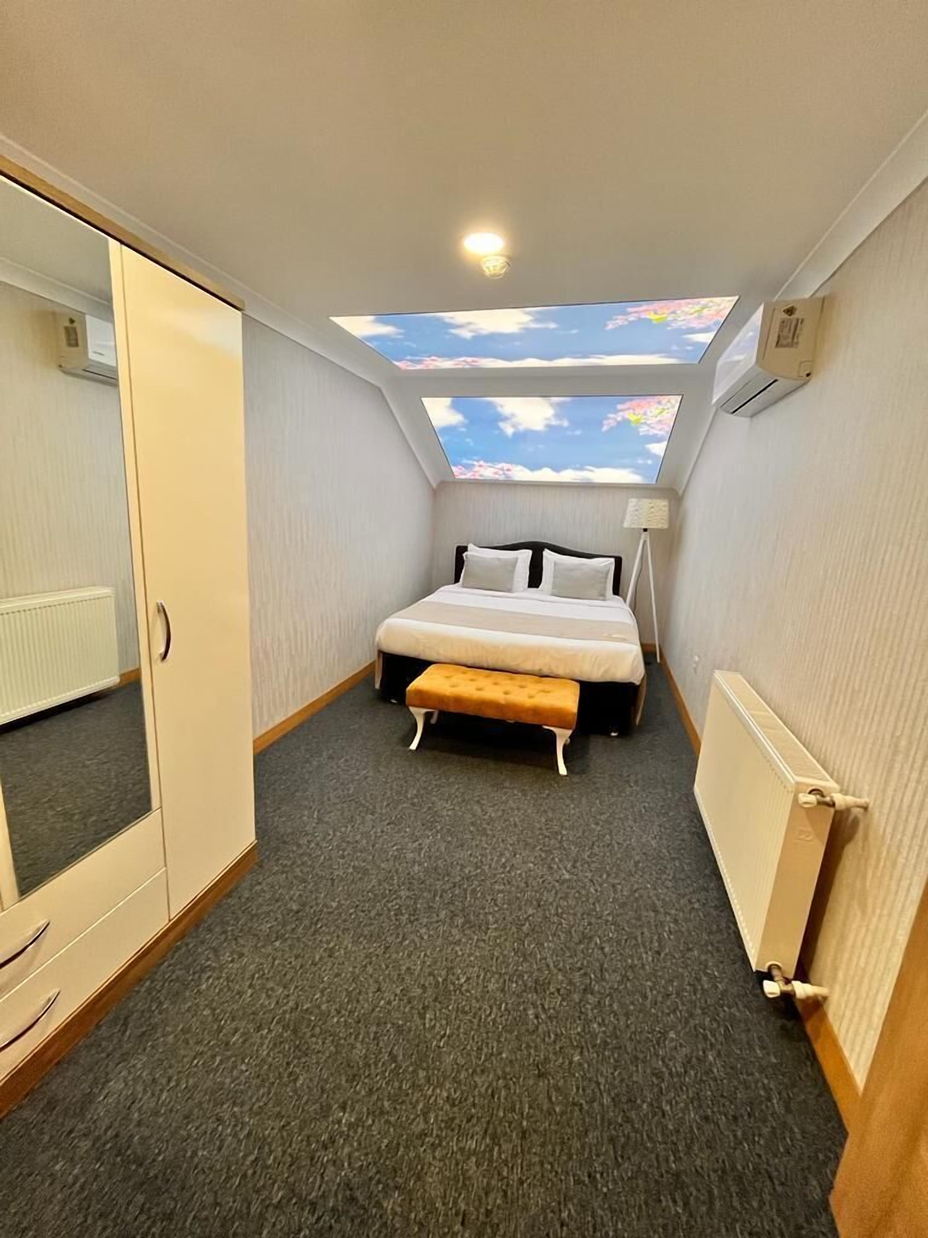 A small, well-lit bedroom with a skylight, a bed, a bench, and a wardrobe.