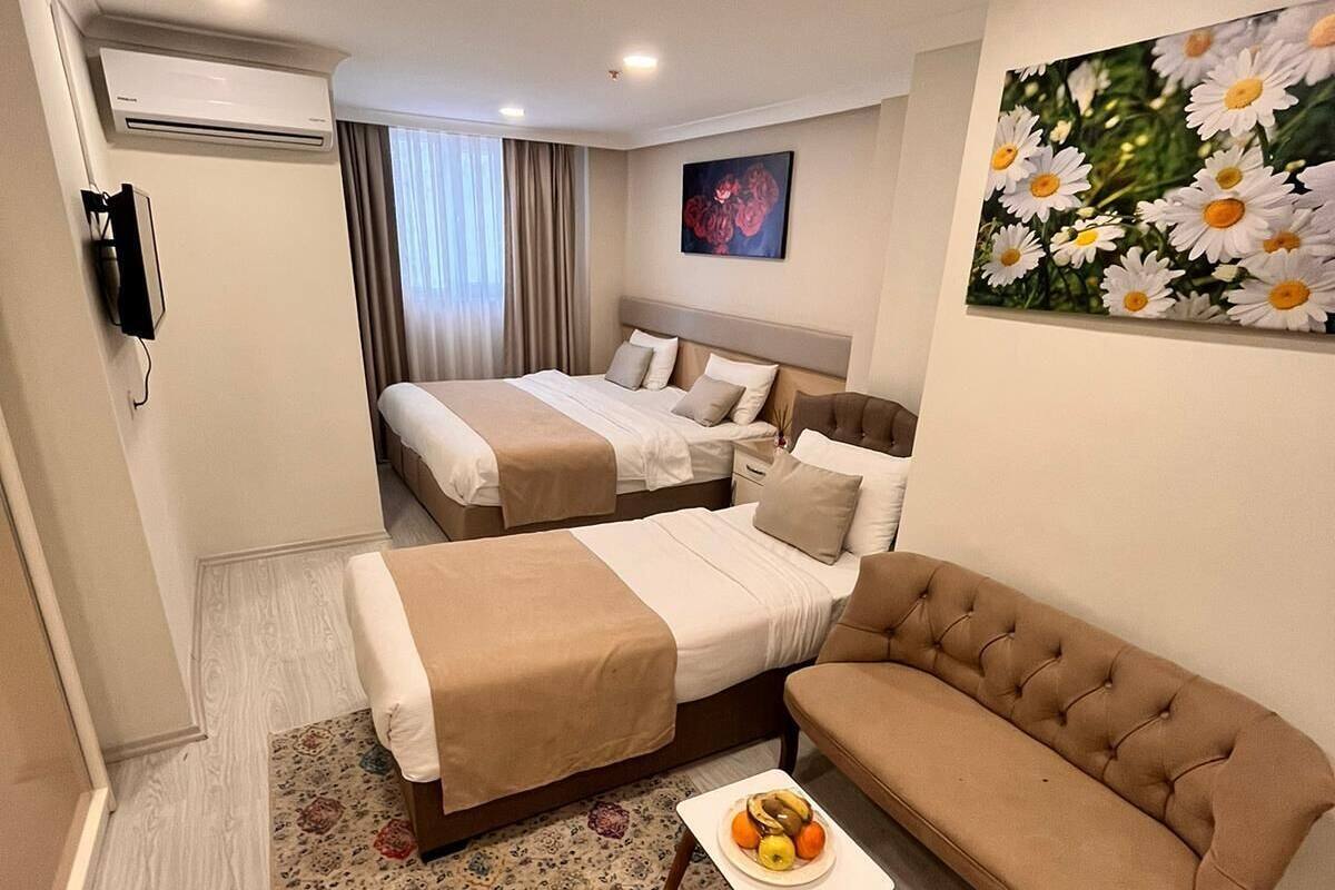 A hotel room with a bed, a sofa, a small table with fruit, and a painting of flowers.