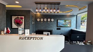 A reception desk with a 'RECEPTION' sign, a clock, a framed picture, and a window with a view. - Şimal Hotel (Rize)