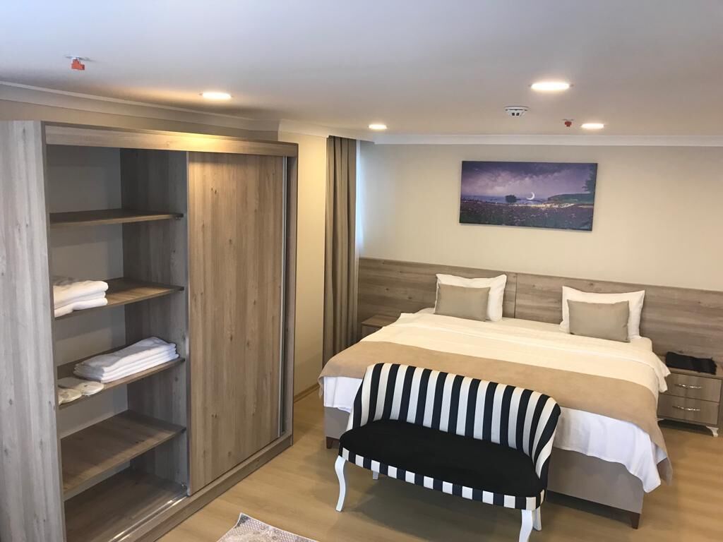 A bedroom with a bed, a bench, a wardrobe, and a painting on the wall.