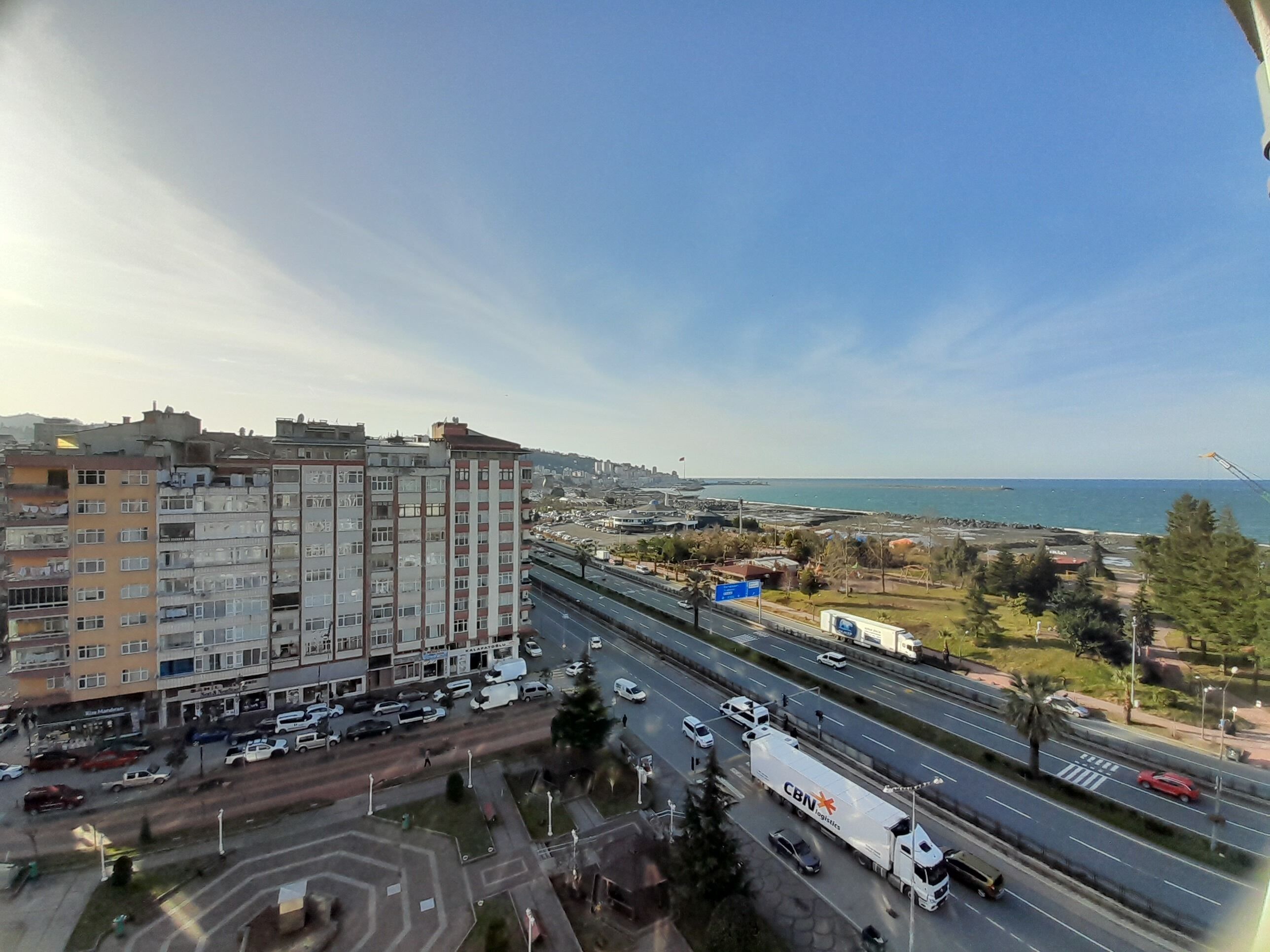 A multi-level building with a mix of residential and commercial spaces, a busy highway with vehicles, and a clear view of the sea in the background.