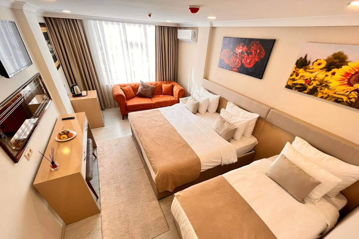 A hotel room with two beds, a sofa, a TV, and artwork on the walls.