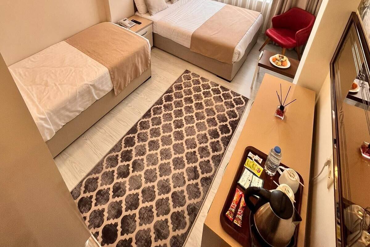 A hotel room with two single beds, a desk with a chair, a small table with a plate of food, and a red chair.