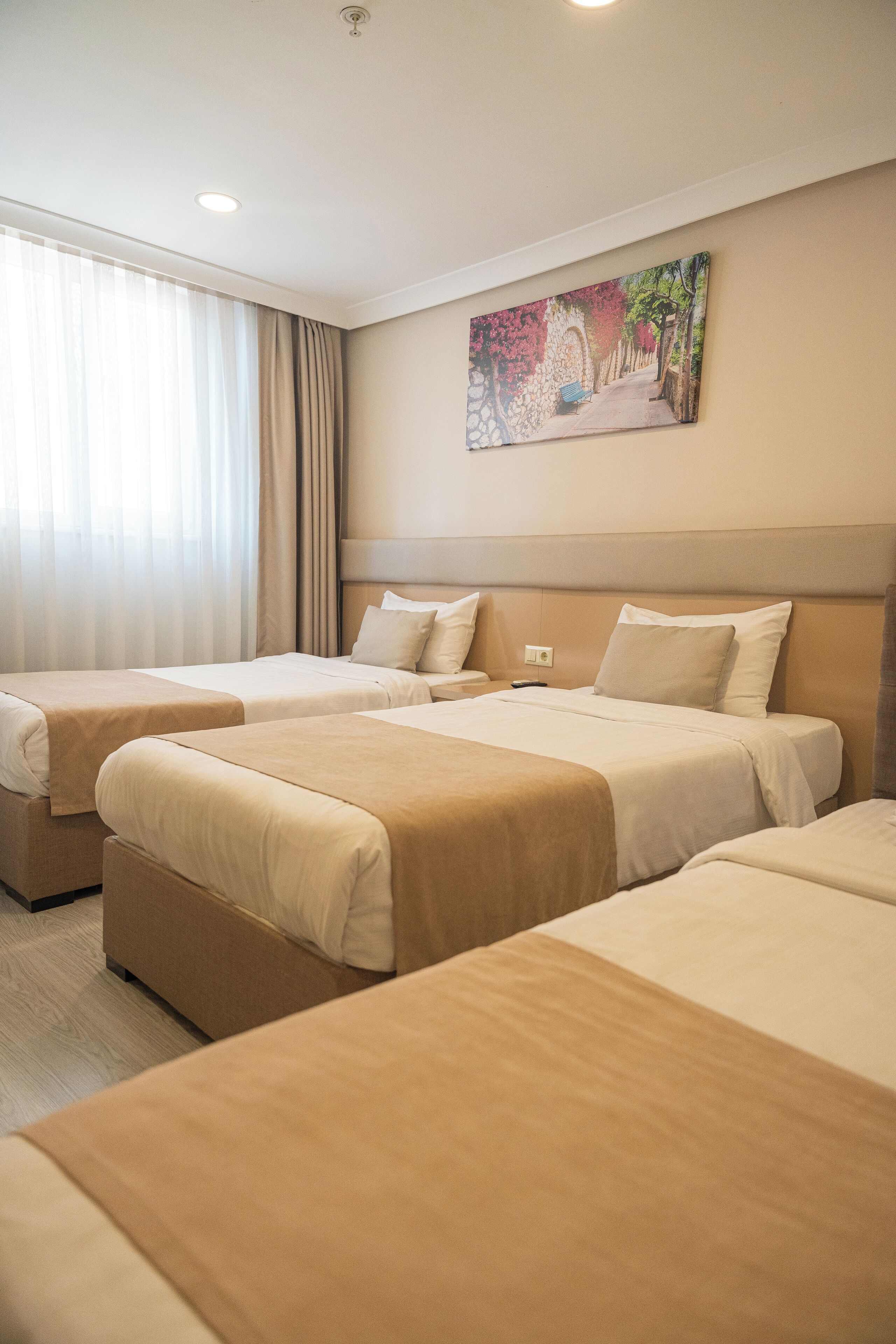 Una camera d'albergo con tre letti, un quadro appeso al muro e una finestra con tende.