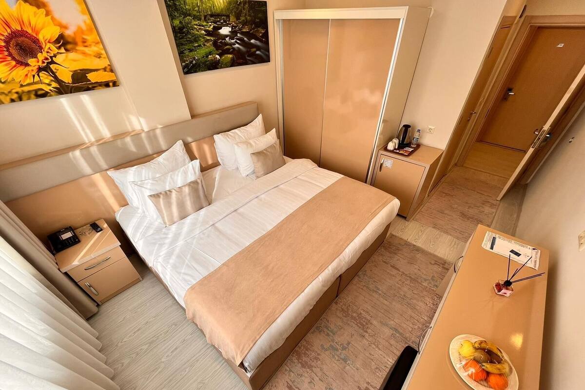 A neatly arranged hotel room with a bed, bedside tables, a desk with a fruit bowl, and a wardrobe.