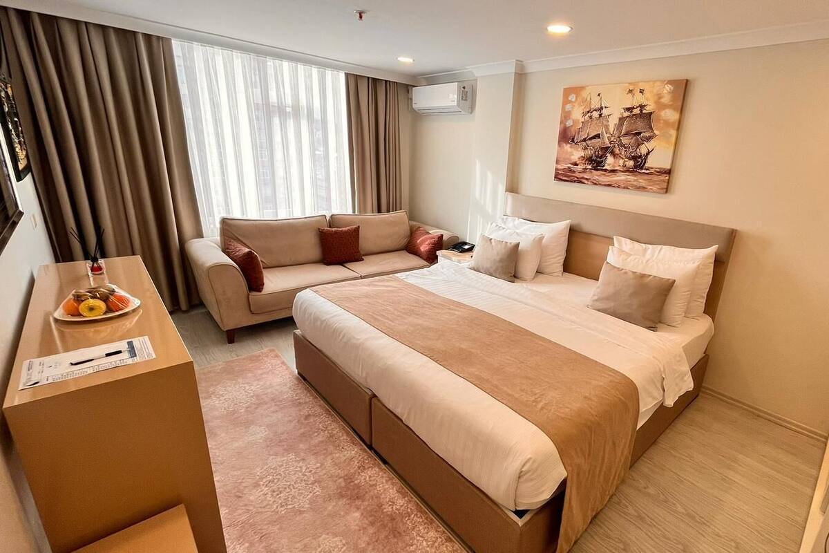 A hotel room with a bed, a sofa, a desk, and a painting on the wall.