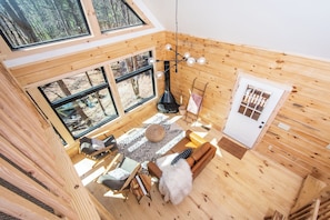 Uma cabana acolhedora com quarto no mezanino, janelas amplas, área de jantar e lareira.