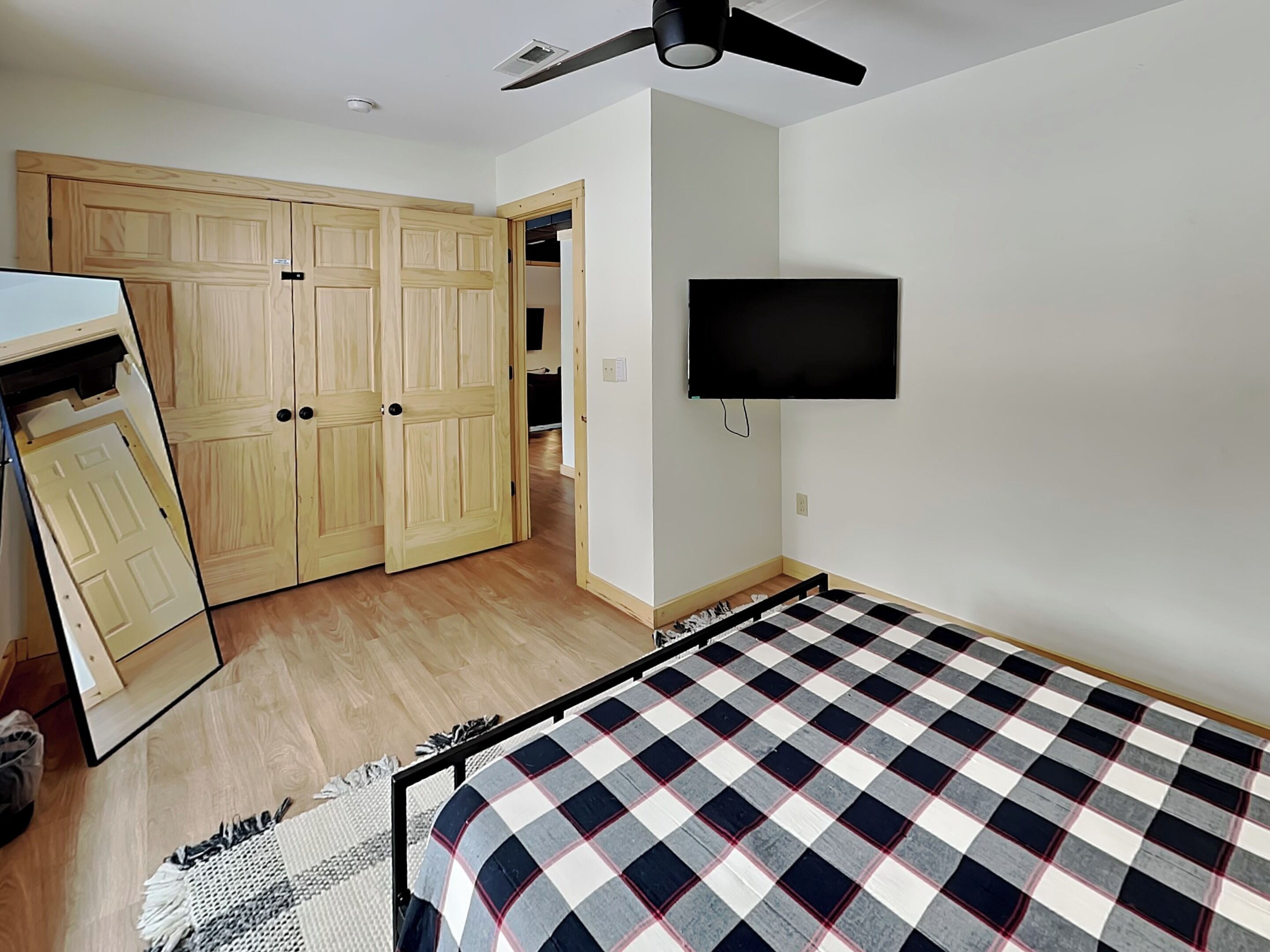 A bedroom with a bed, a wardrobe, a television, and a ceiling fan.